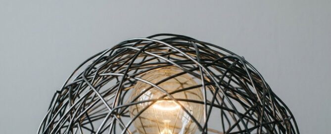 Lampadina accesa intrappolata in una struttura metallica intrecciata, metafora del perfezionismo che genera blocco mentale nel Business English.