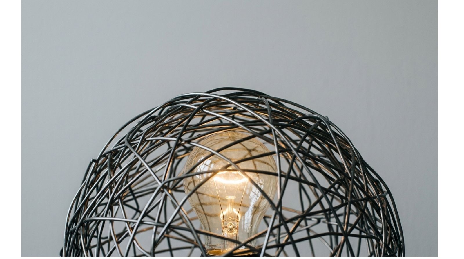 Lampadina accesa intrappolata in una struttura metallica intrecciata, metafora del perfezionismo che genera blocco mentale nel Business English.