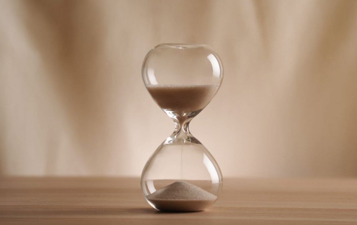 Clessidra in vetro con sabbia che scorre su un tavolo di legno, simbolo di gestione del tempo, scadenze e time management.