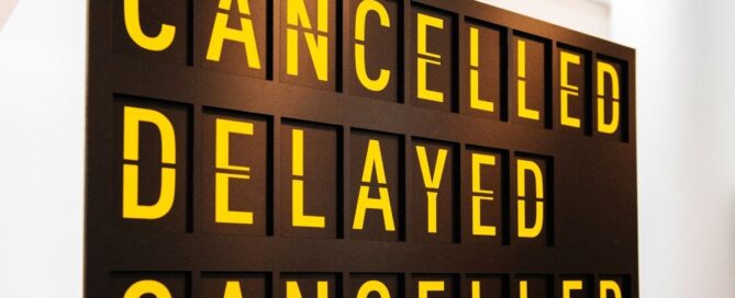 Tabellone degli arrivi e partenze con le scritte in giallo Cancelled e Delayed su sfondo nero, metafora di un imprevisto di Business English durante un viaggio di lavoro.