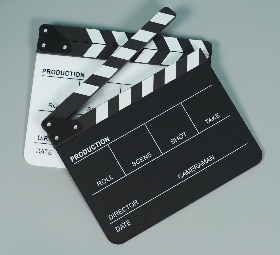 Due ciak cinematografici, uno bianco e uno nero, incrociati su sfondo grigio, usati come prompt visuale per gestire gli imprevisti e rifare la scena nel Business English.