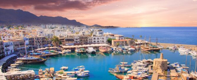 Porto turistico di Kyrenia a Cipro con barche ormeggiate al tramonto, banner rosso in alto a sinistra e testo Holiday English per l'articolo del blog.