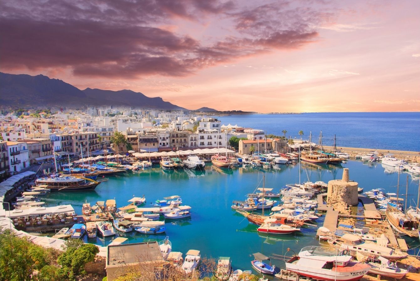 Panoramica dall'alto del porto di Cipro con imbarcazioni e case affacciate sul mare turchese, usata come esempio di imprevisti durante il check-in in hotel.