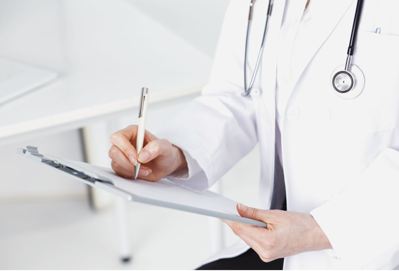 Medico in camice bianco con stetoscopio che compila una cartella clinica, a corredo della sezione sulle piccole emergenze mediche e farmacia all'estero.